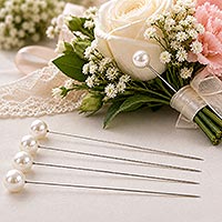 Pearl-headed corsage pins displayed beside an elegant bouquet of white roses, baby's breath, and pink carnations, illustrating their use in floral arrangements, corsages, boutonnieres, and wedding crafts.
