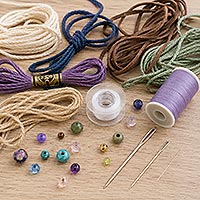 Close-up of assorted cord and thread stringing materials including leather cord, waxed cord, embroidery floss, clear beading thread, sewing thread, decorative beads, and beading needles for jewelry making and crafts.