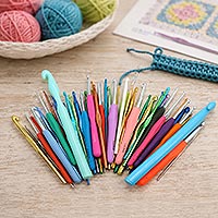 Collection of crochet hooks in different styles, sizes, and materials displayed on a craft table with yarn, a crochet project, and a crochet pattern, illustrating the wide variety of crochet hooks available.
