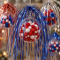Patriotic fillable ornament craft featuring red, white, and blue pom poms with metallic foil streamers for Independence Day and Fourth of July decorations.